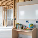 “Child-height learning desk with books and building blocks in an open-plan unfinished renovation space, beside planned shelving and visible electrical outlets.”